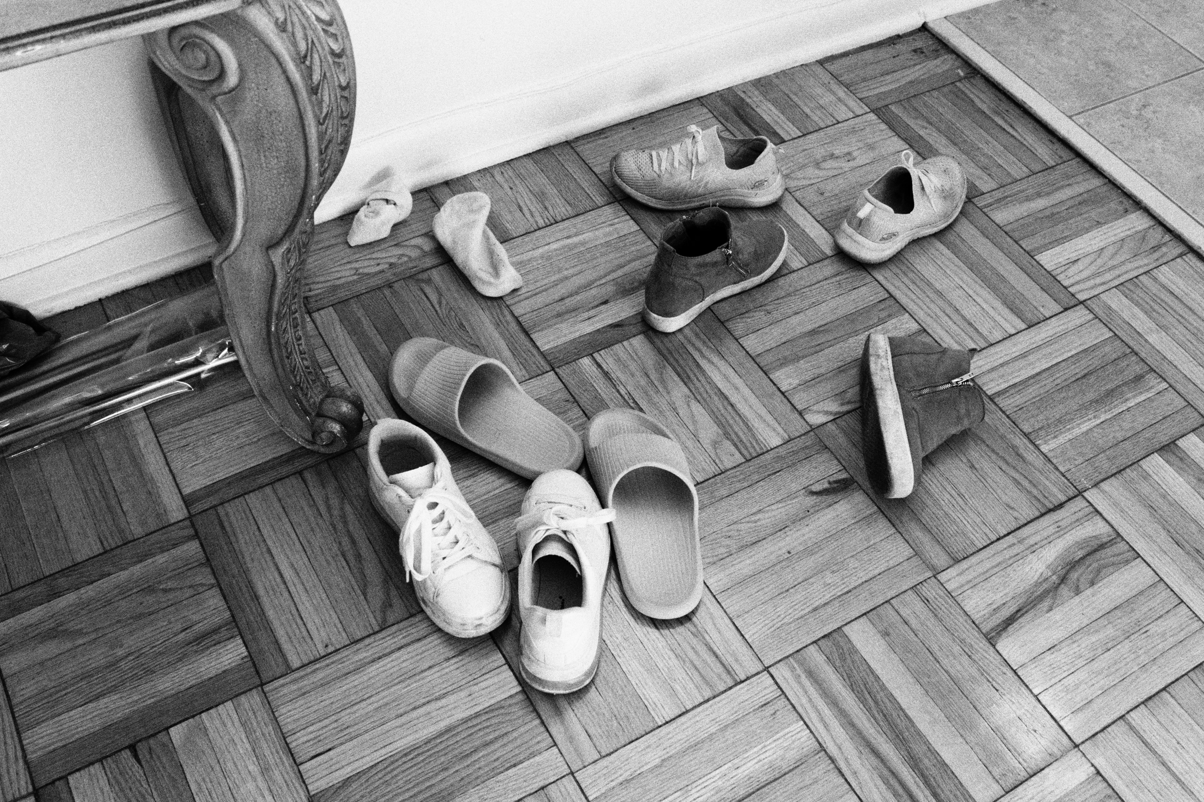 Black-and-white photograph — shoes and slippers arranged on a plank floor