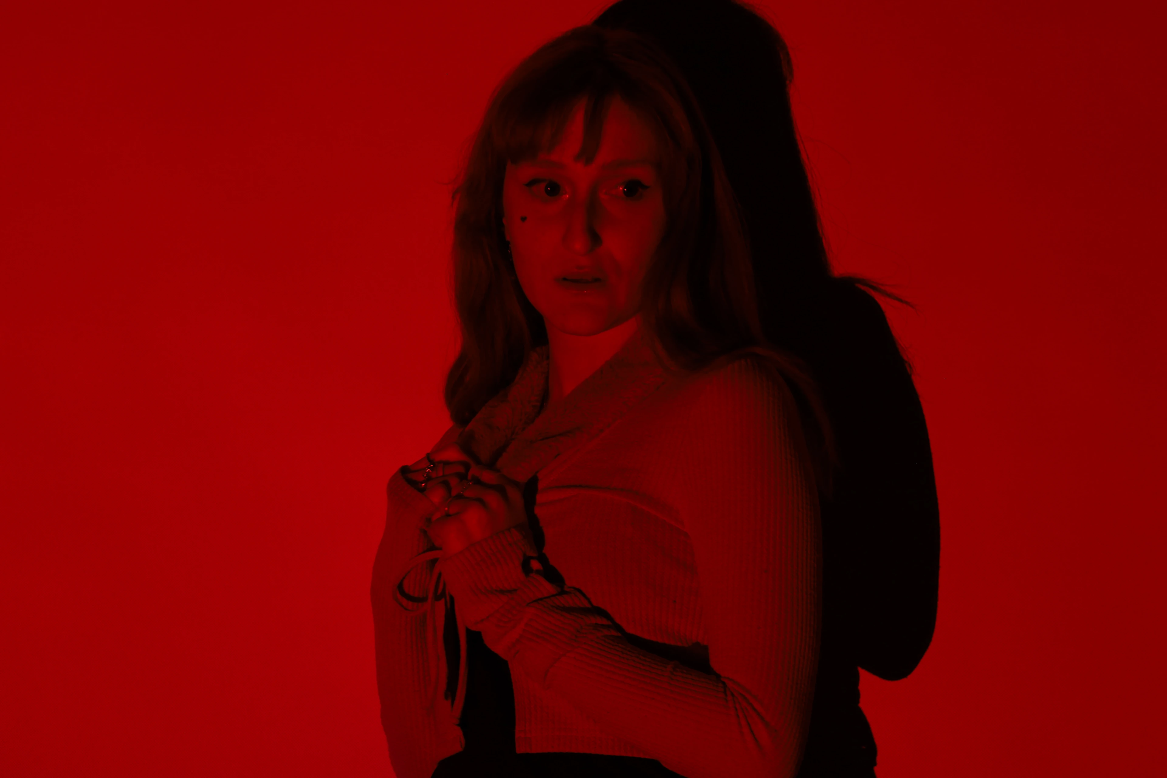 Photograph — a red-haired woman lit in deep red, hands clasped