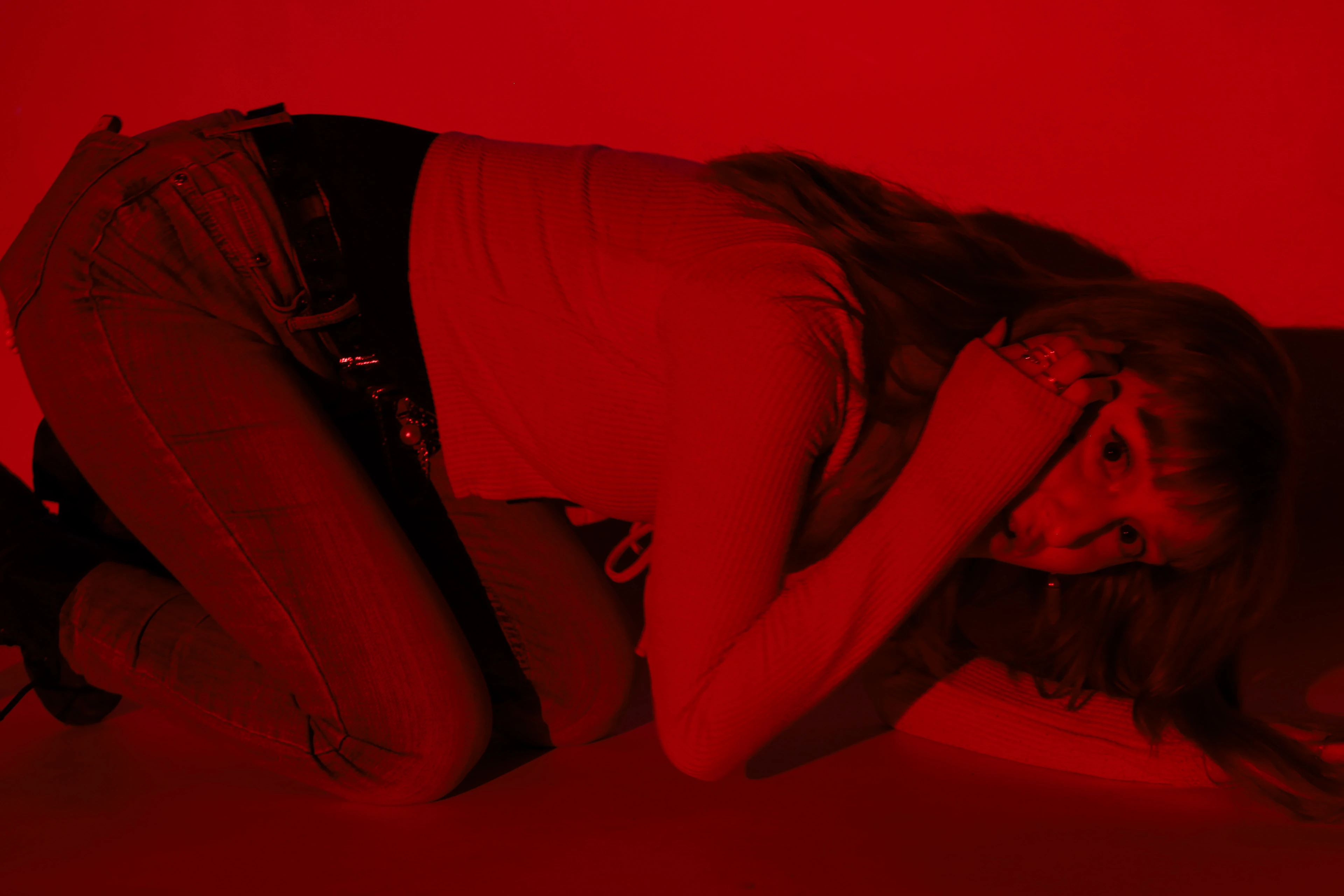 Photograph — a woman curled on the floor under red light