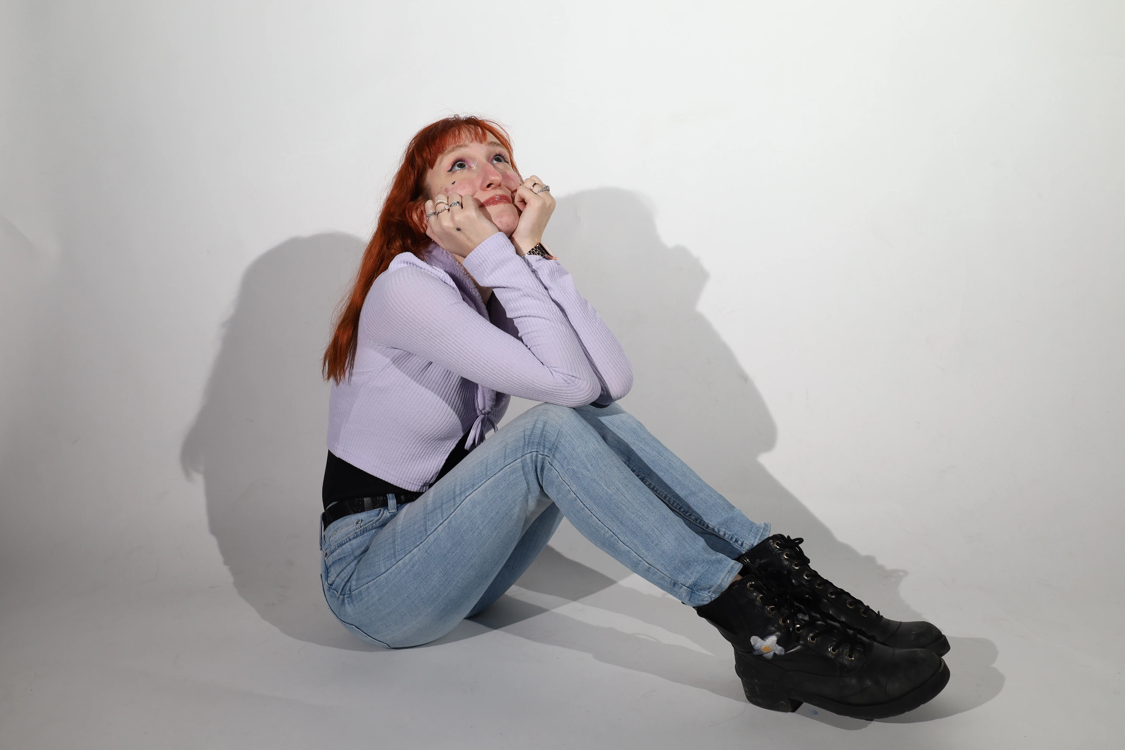 Studio portrait — a woman in a lilac top and jeans sitting against a white wall