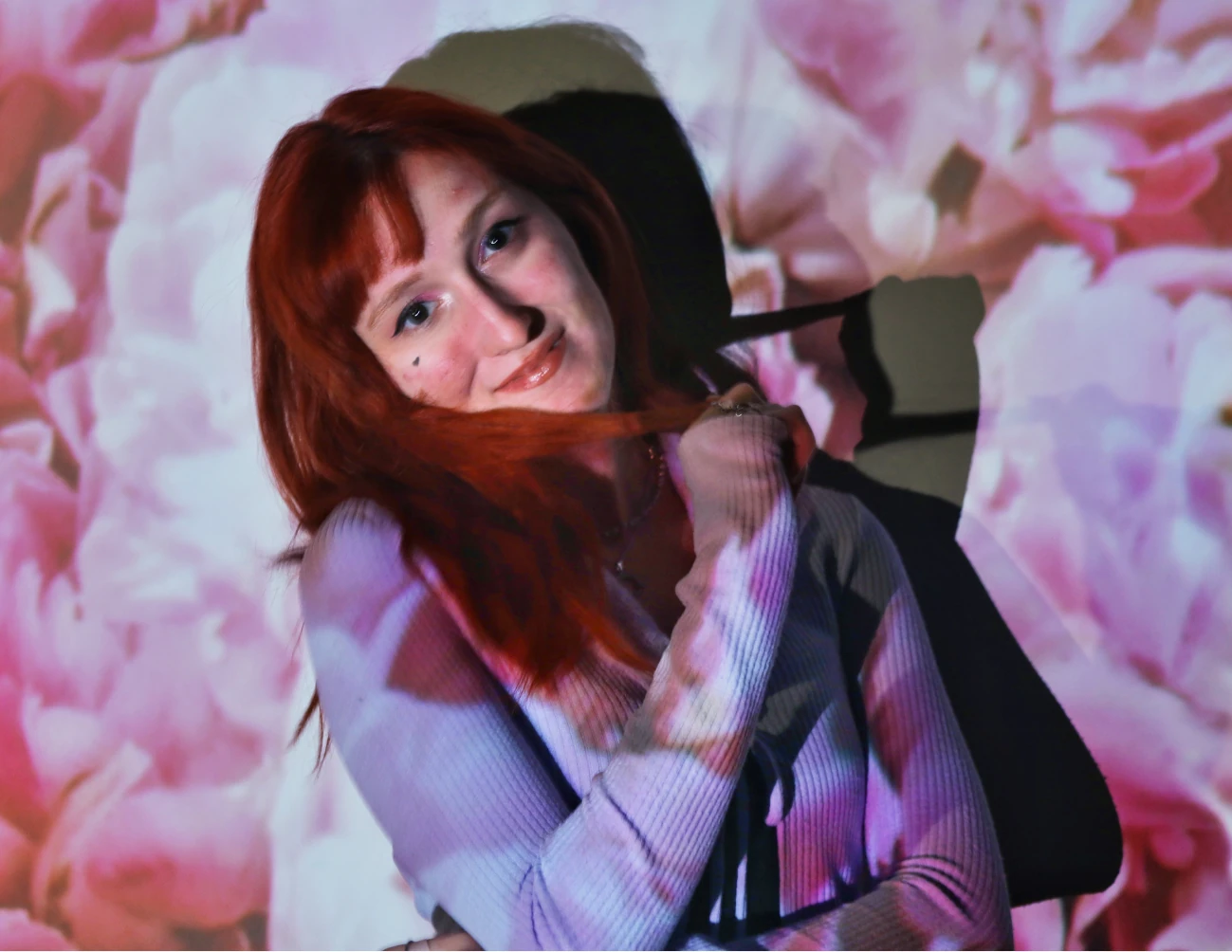 Photograph — a red-haired woman smiling through a pink blossom light projection