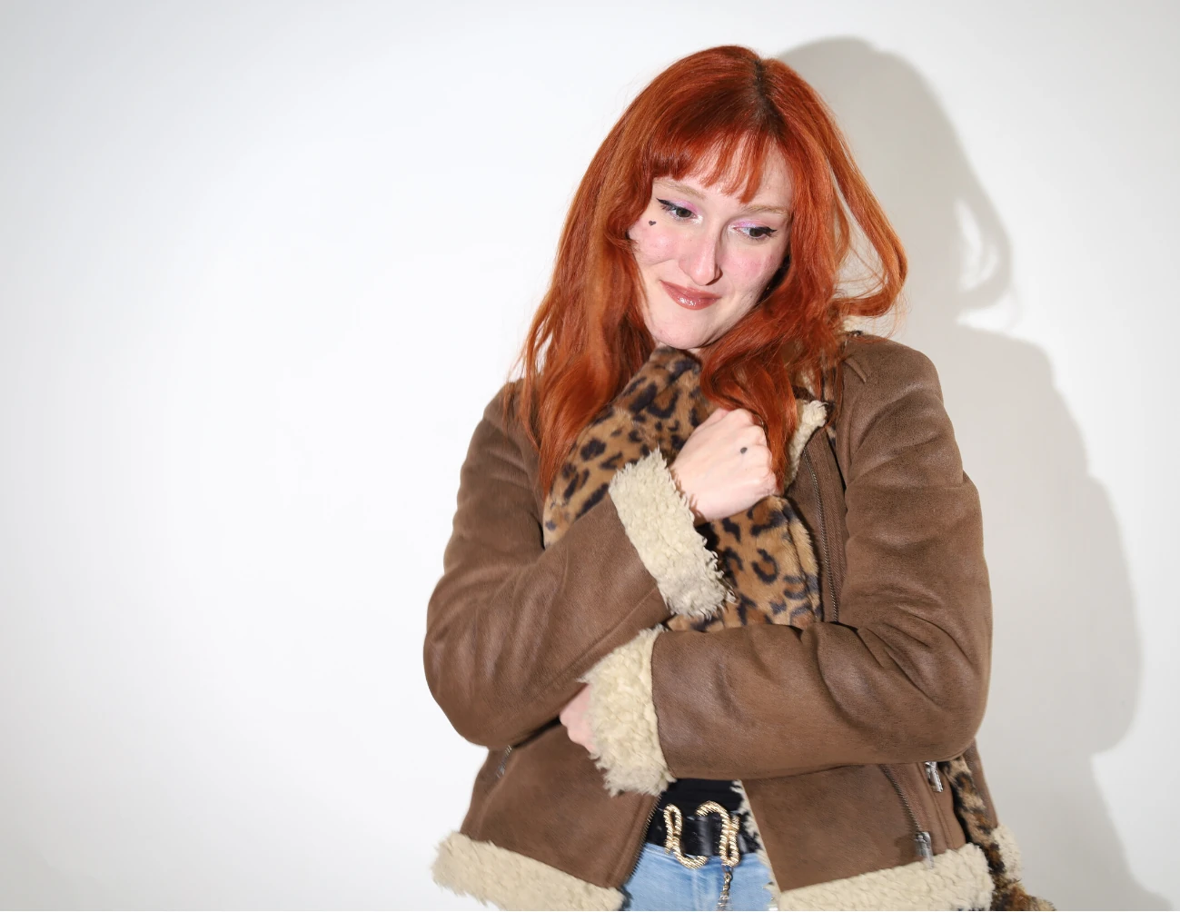 Studio portrait — a woman in a shearling jacket with arms crossed on a white backdrop