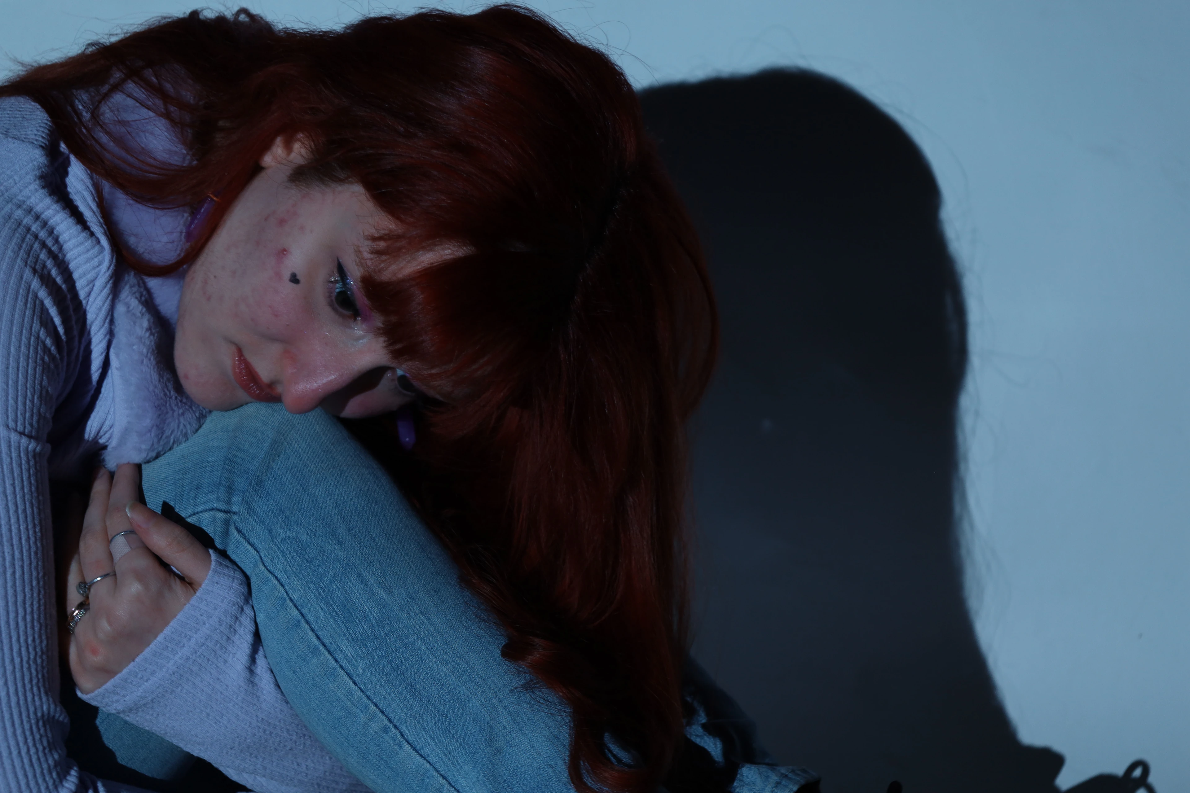 Photograph — a woman resting her head on her knees against a blue-grey backdrop