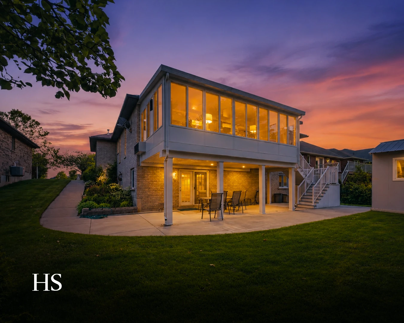 Dusk rear view of the raised bungalow with its sunroom lit against an orange and purple sunset