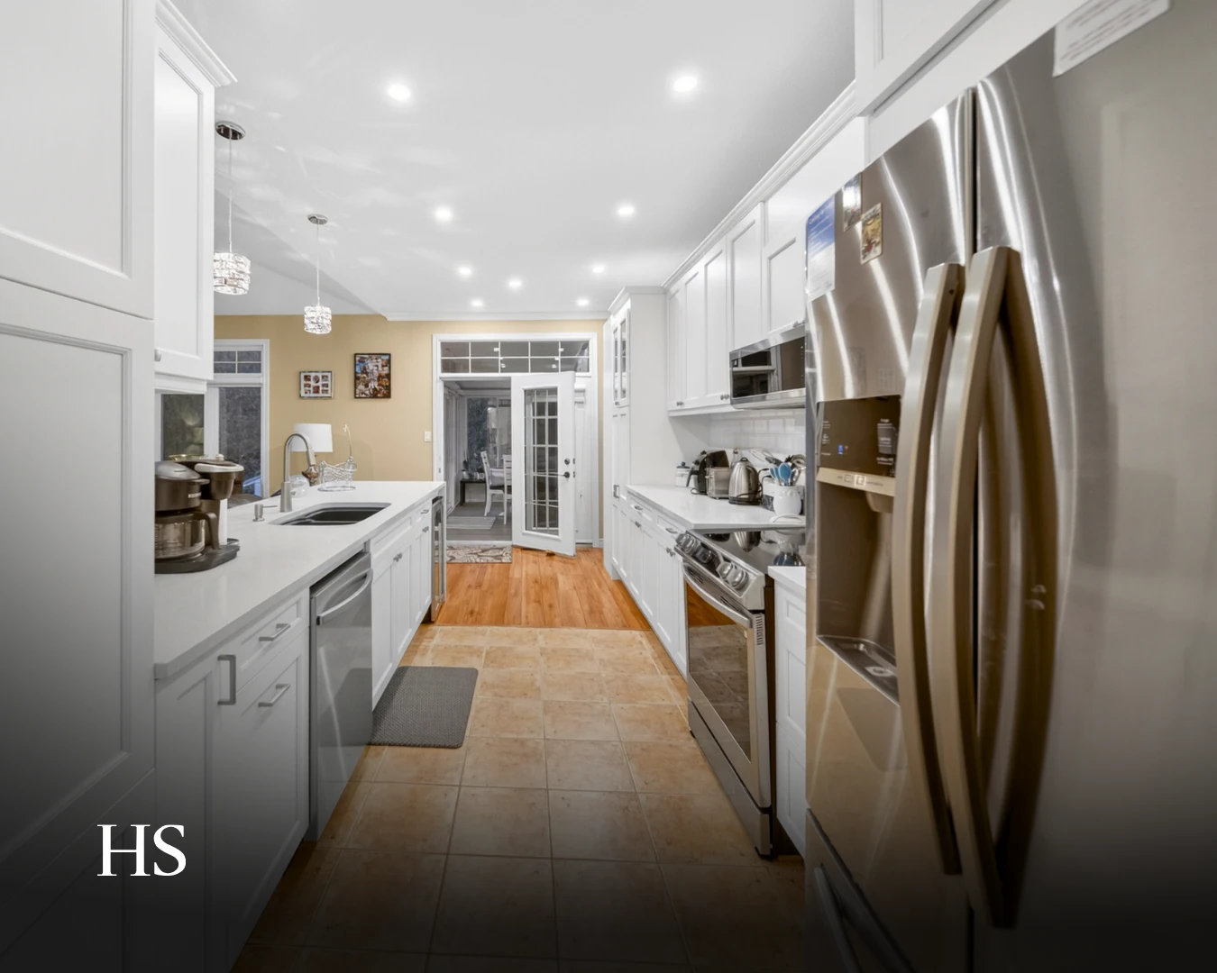 Galley kitchen with white cabinetry, a stainless fridge and oven, and pendant lights over the counter