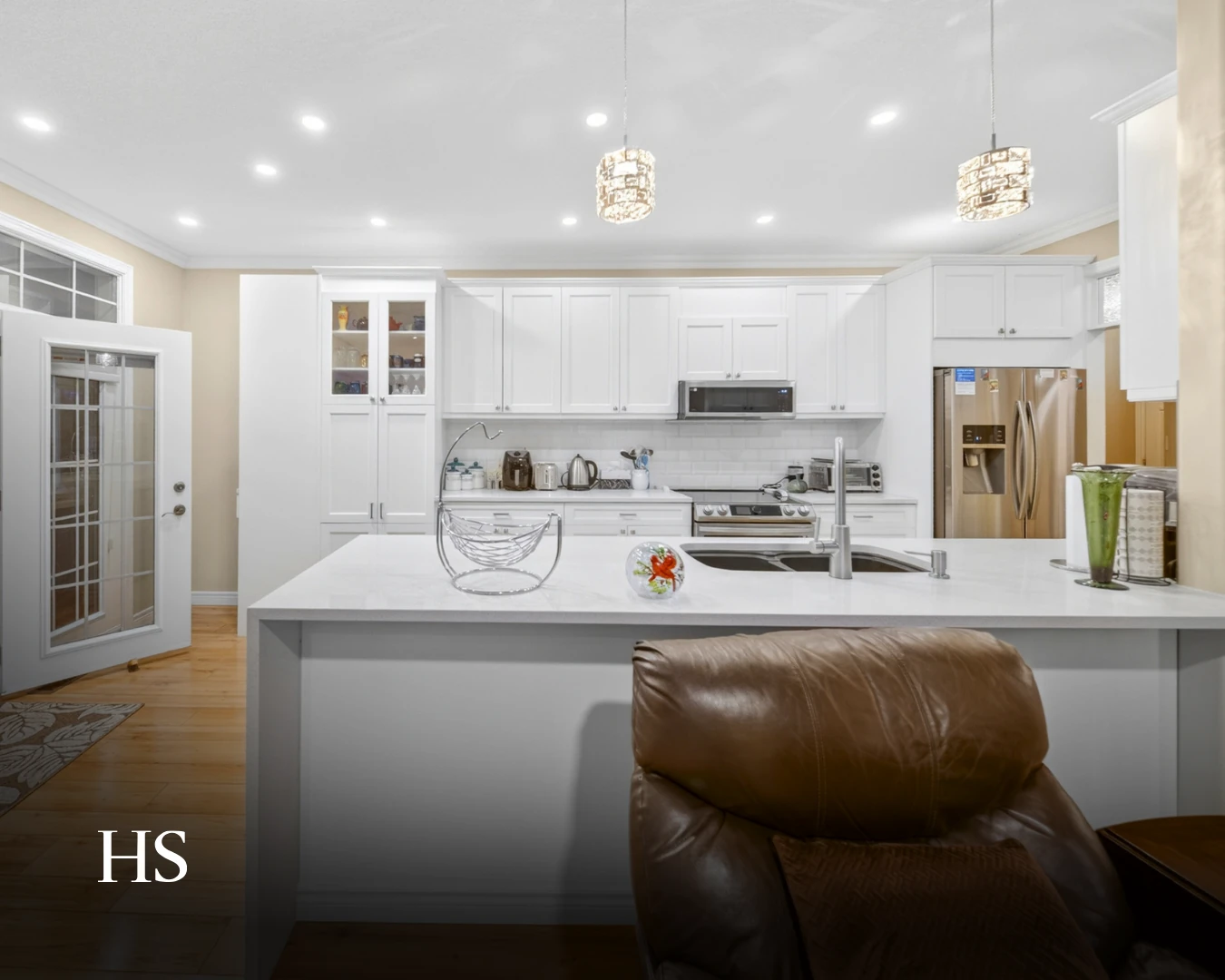 Kitchen with a quartz island, pendant lights and a stainless range hood, with a brown leather chair at the counter