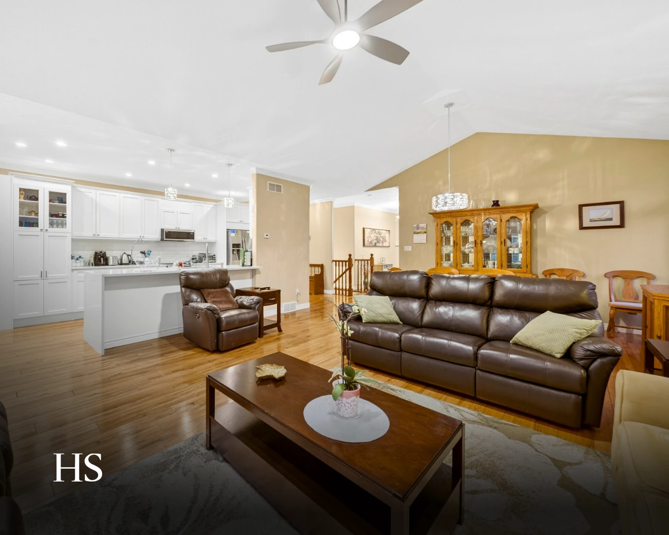Open-plan living room with a brown leather sofa and recliner, opening onto the white kitchen