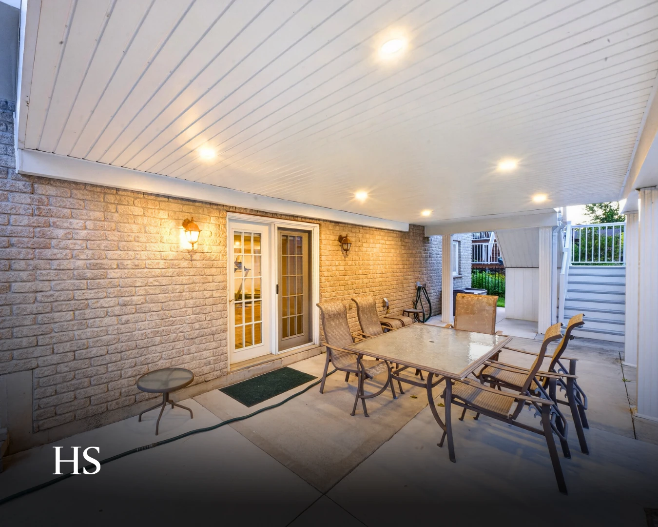 Covered brick patio at dusk with a patio set and a beadboard ceiling of recessed lights
