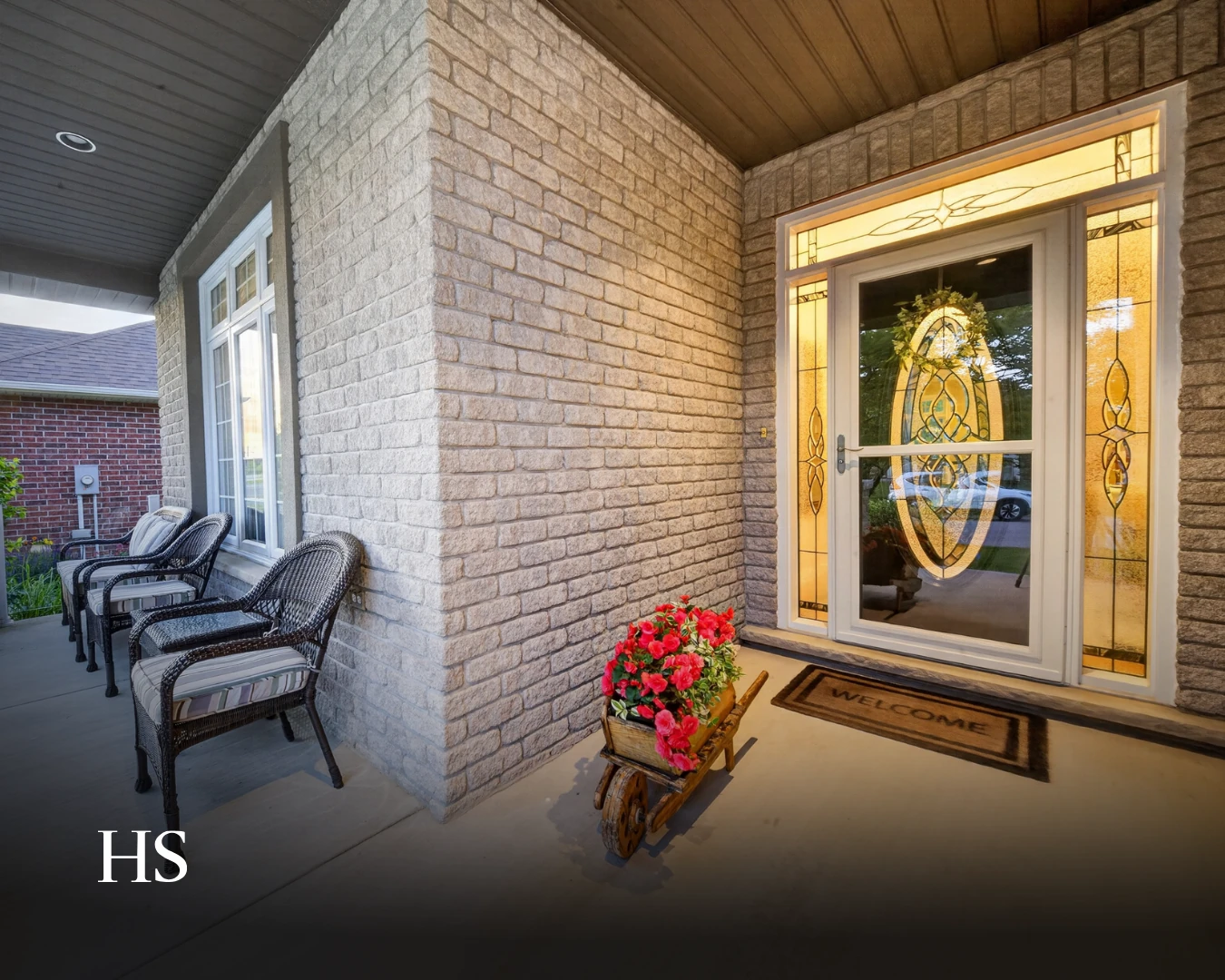 Covered porch with a decorative glazed front door, potted flowers and wicker chairs