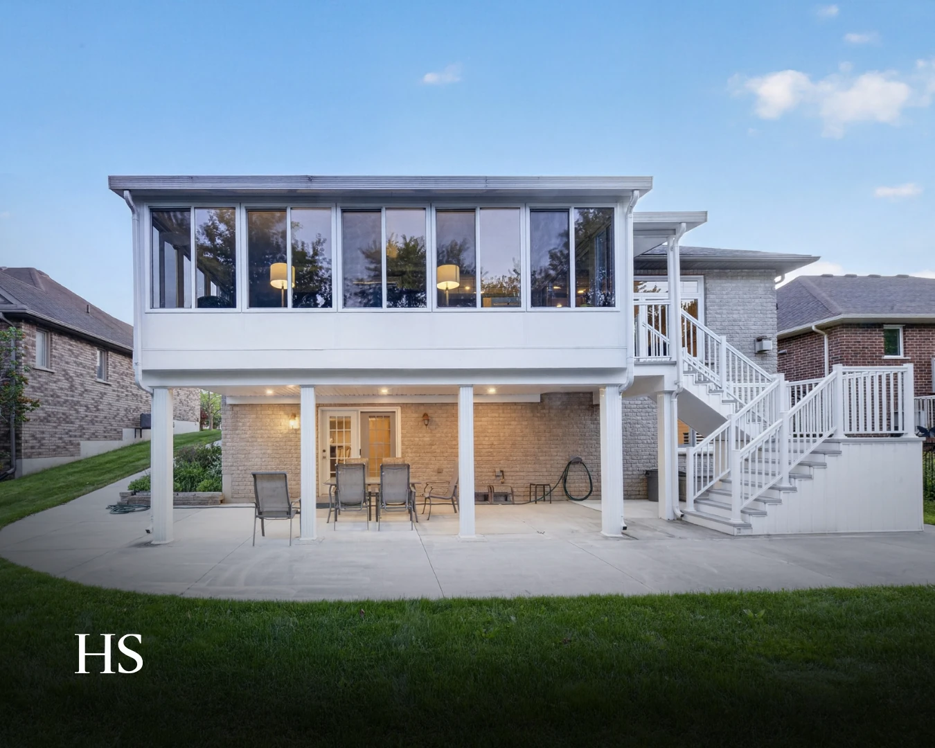 Rear elevation in daylight, showing the white sunroom, the deck and the steps to the yard