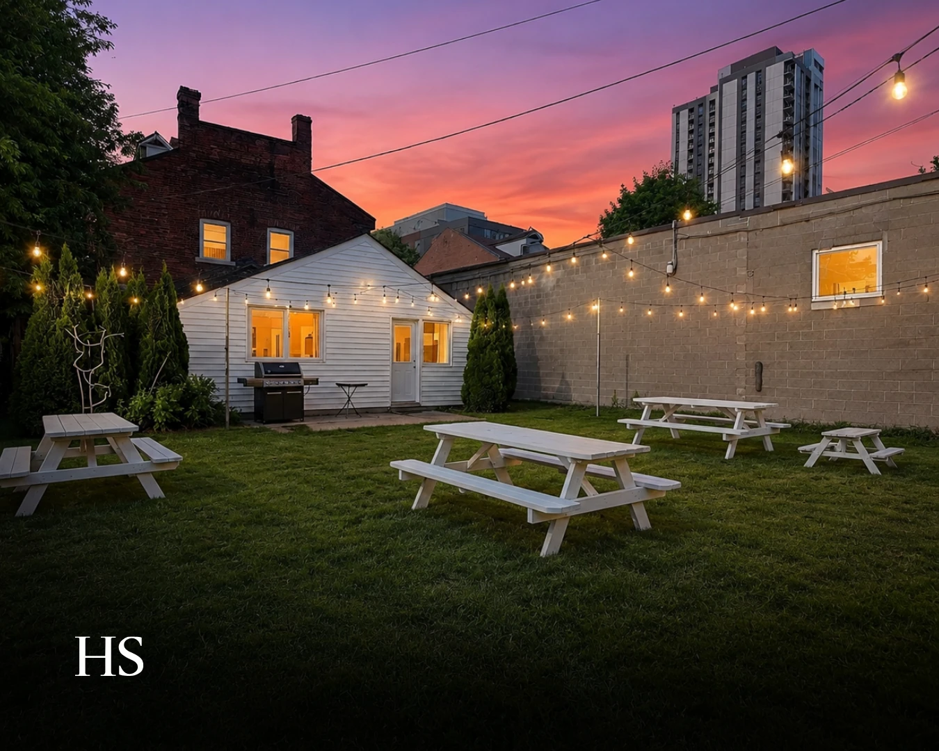 Rear courtyard at sunset with string lights and white picnic tables on the lawn