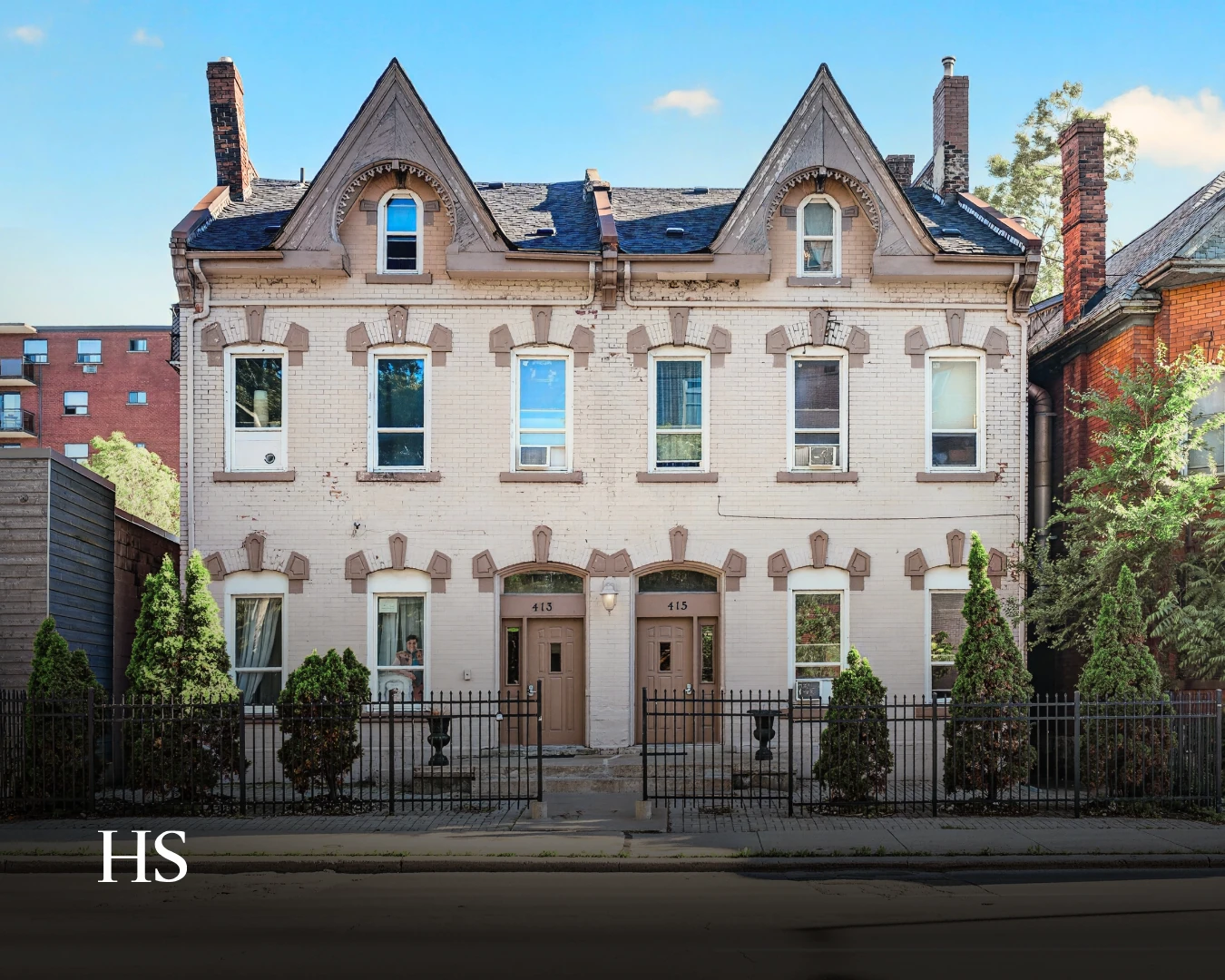 Full daylight elevation of the white-brick semi with twin gables and a black wrought-iron fence