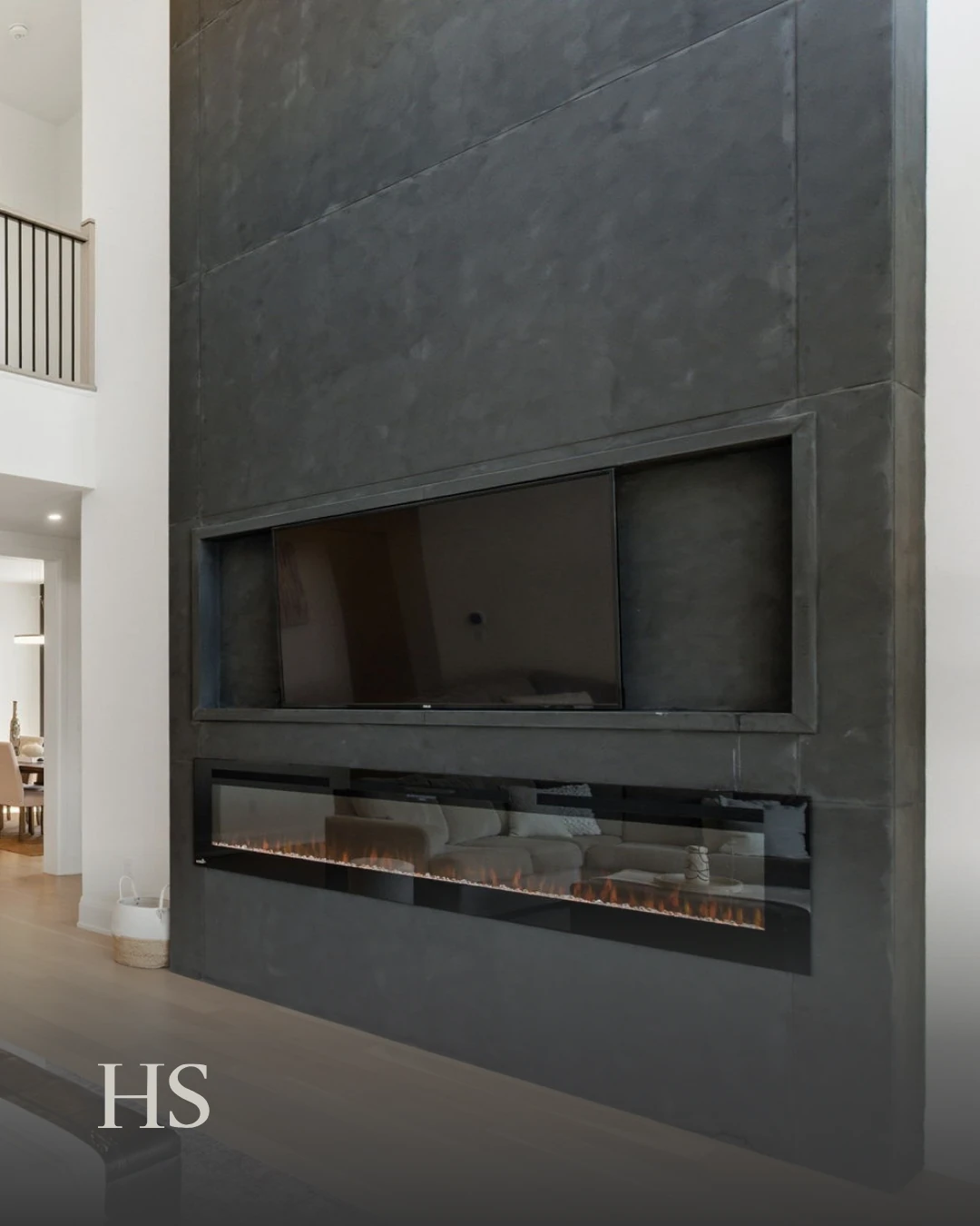 Floor-to-ceiling charcoal concrete fireplace wall with a linear gas flame and a TV niche
