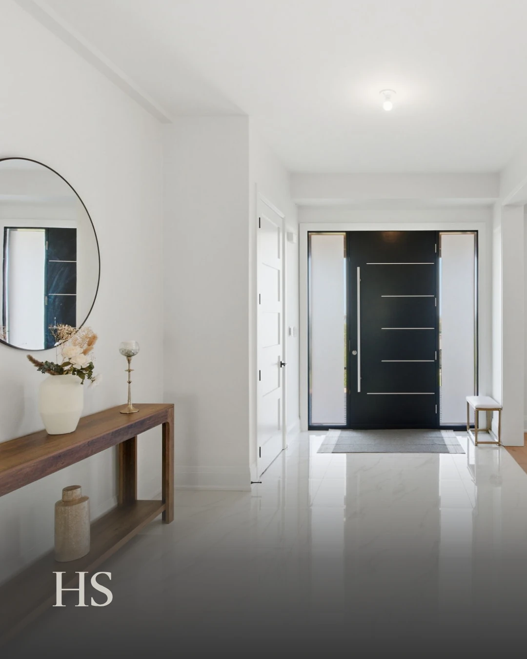 Entry hall with a wood console, a vase of stems, a round mirror and the front door beyond