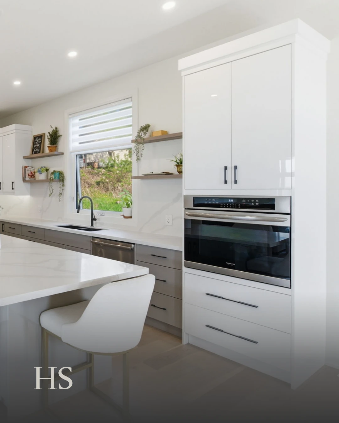 White kitchen with a wall oven in a tall white cabinet, a quartz island and one leather bar stool
