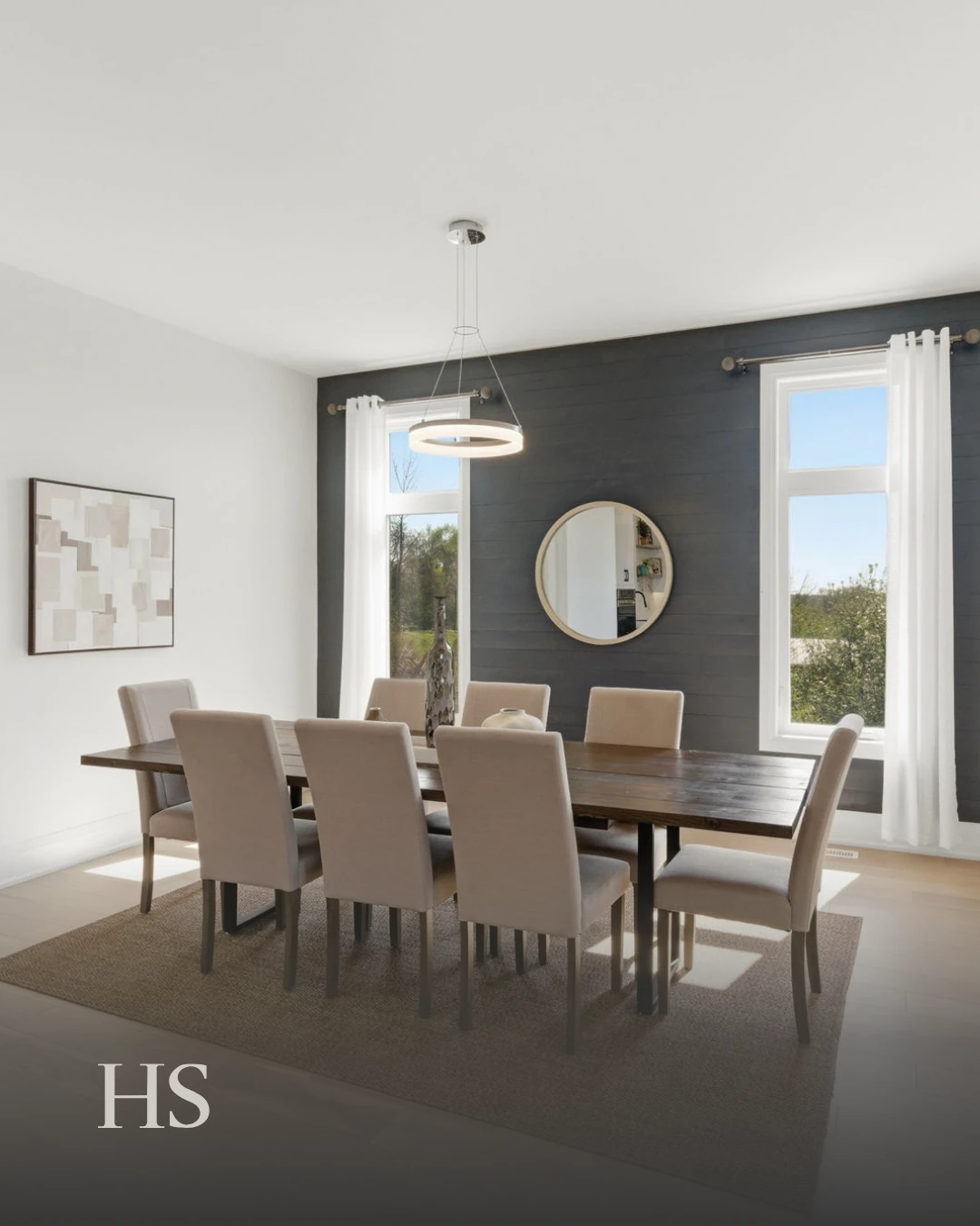 Dining room with a dark accent wall, a round mirror and a table laid for six