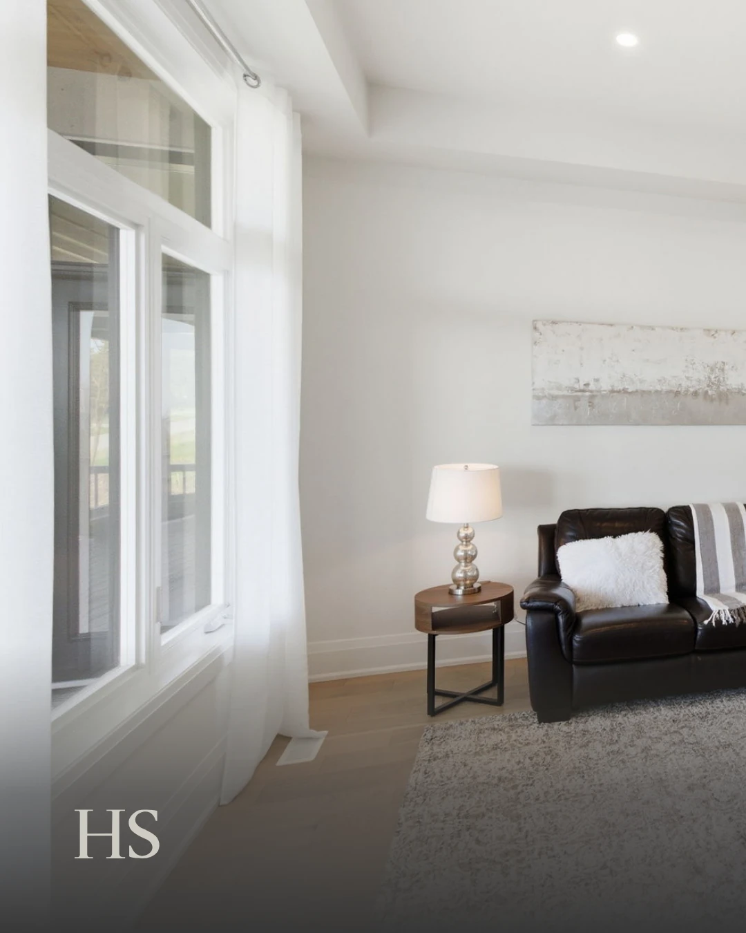 Sitting room with a black leather armchair, a table lamp and tall windows onto the trees