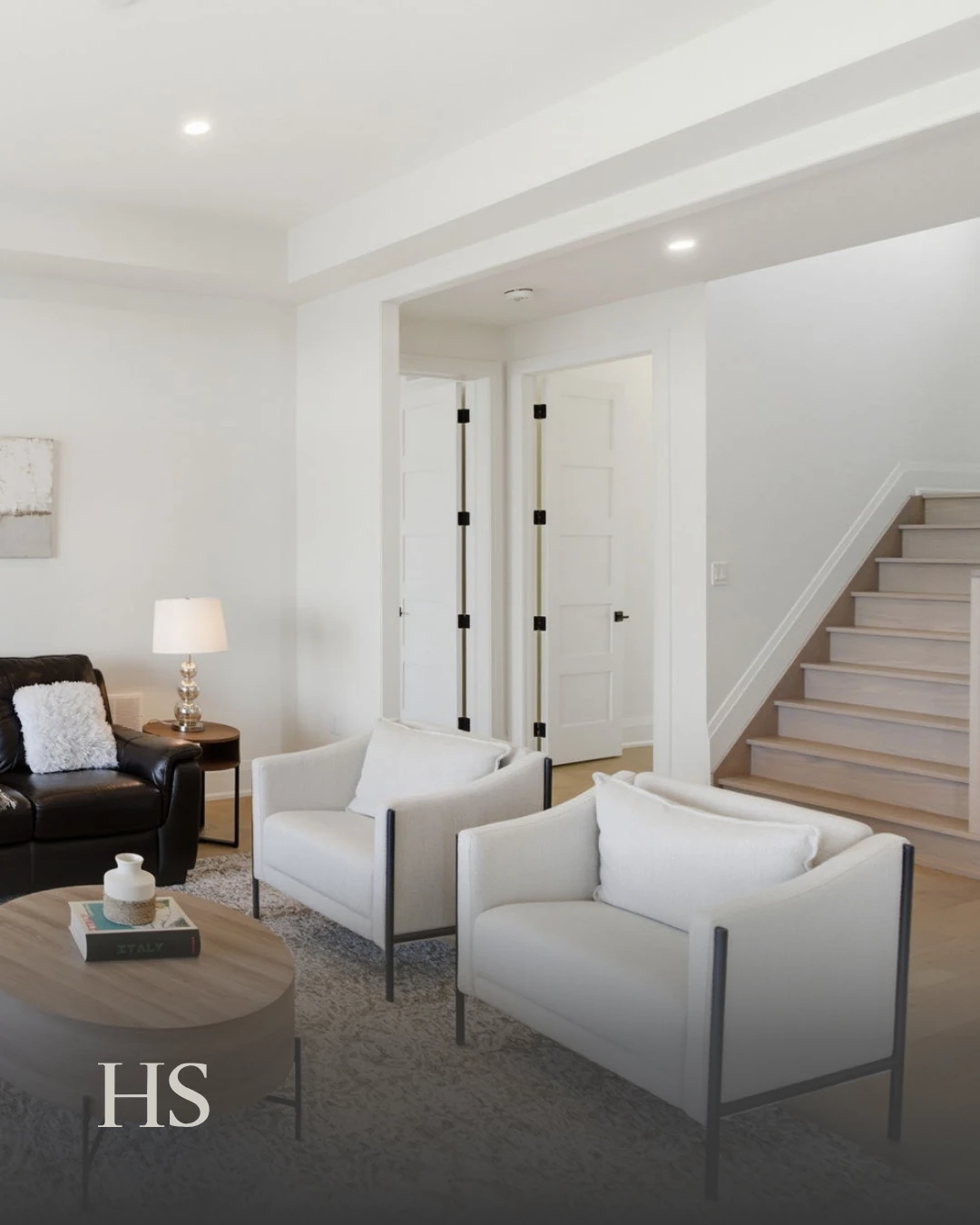 Open-plan sitting area with pale armchairs and a staircase with a glass balustrade