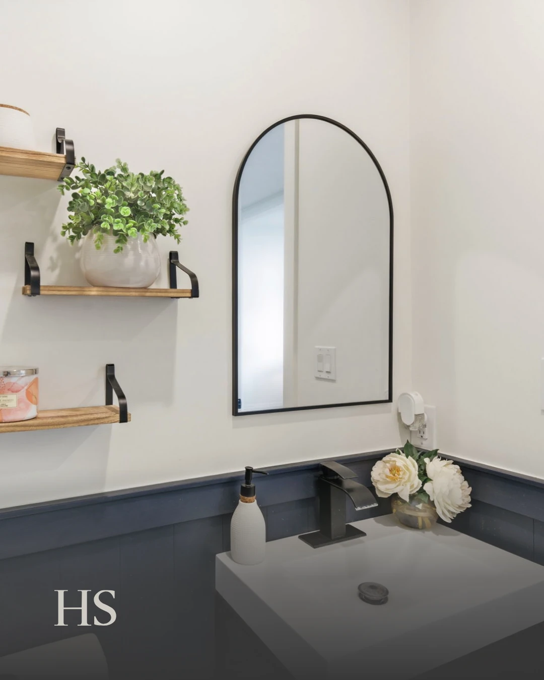 Powder room with a navy vanity, an arched mirror and a potted plant on a timber shelf
