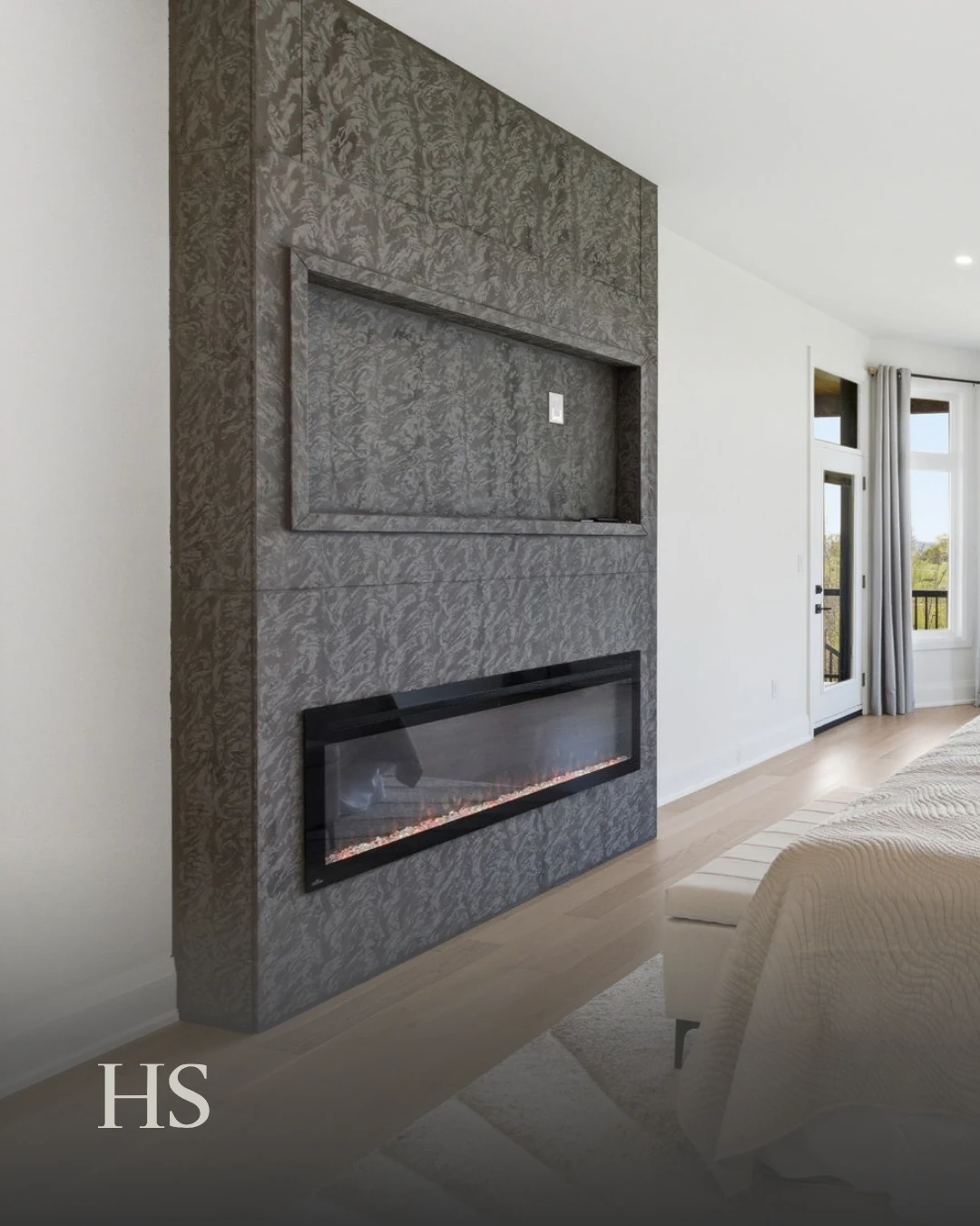 Bedroom with a dark stone fireplace wall and a bed dressed in grey