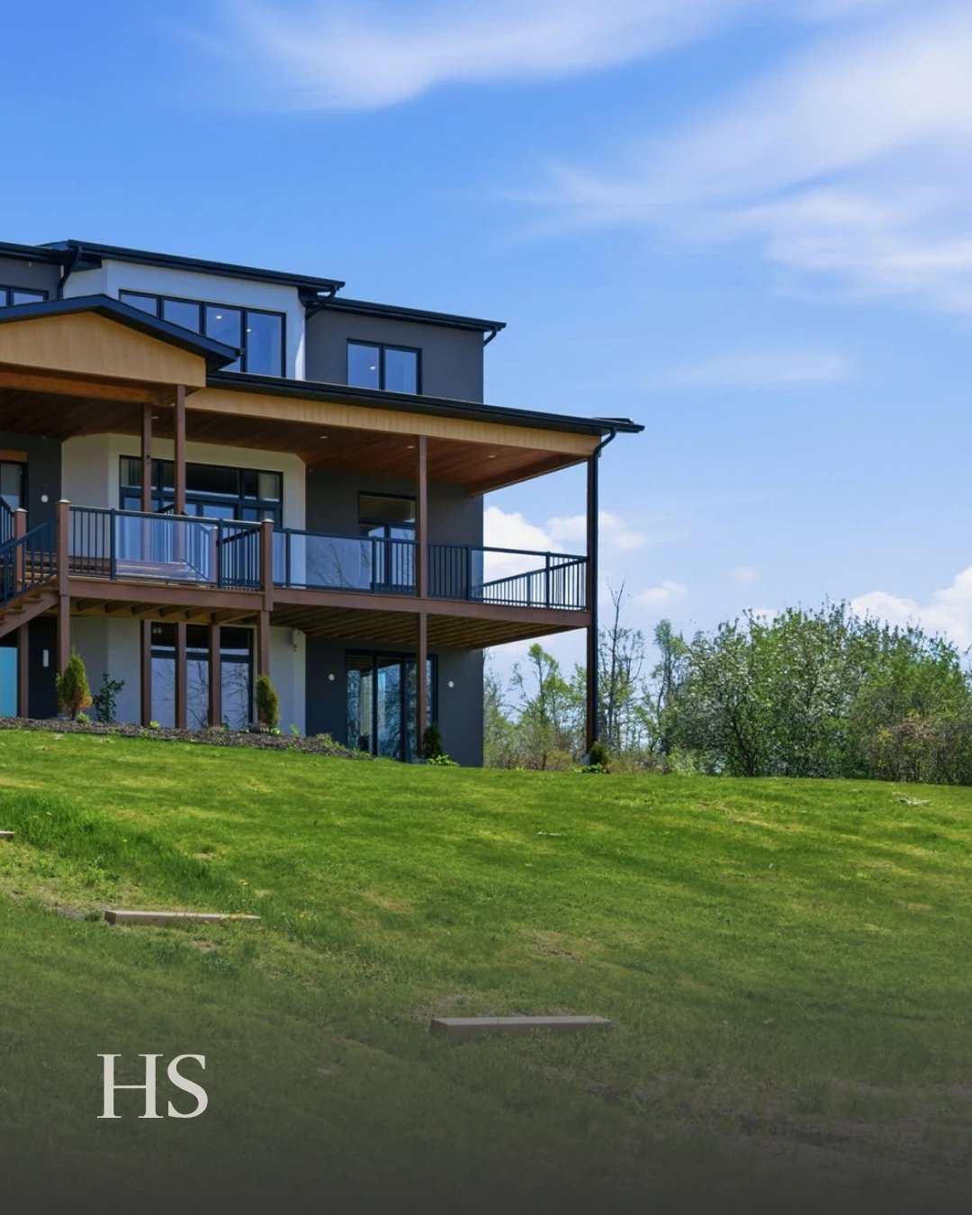 The charcoal and white home rising from its sloping lawn, with a wood-canopied balcony above tall black-framed windows