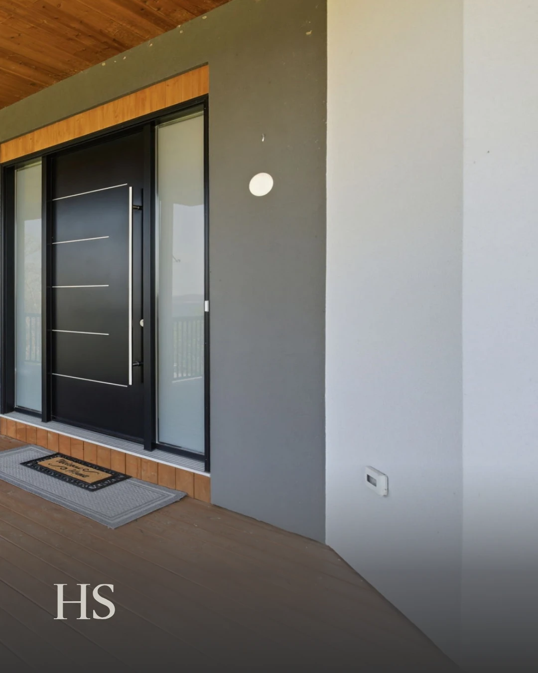 Entrance under a wood ceiling with a dark-framed glass door and a doormat